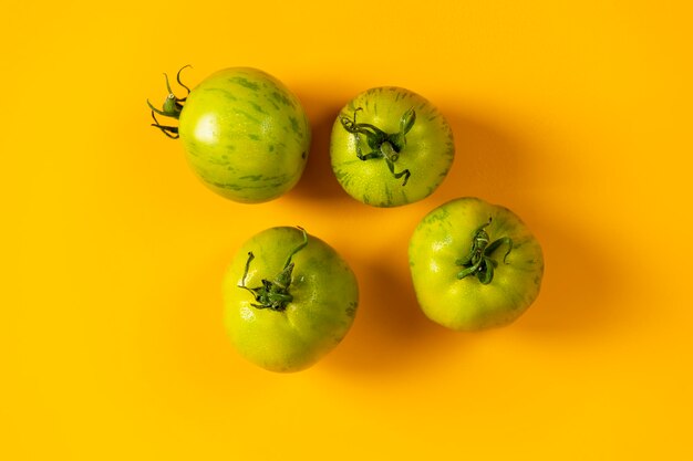 Diferentes tomates rayados verdes frescos crudos sobre fondo amarillo