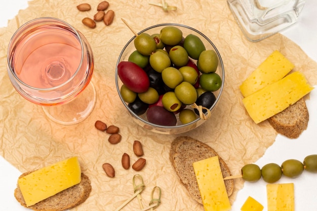 Diferentes variedades de aceitunas en un recipiente de vidrio Copa de pan de vino rosado con queso en papel