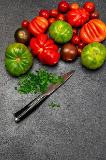 Diferentes variedades de tomates rojos y verdes Perejil picado y cuchillo