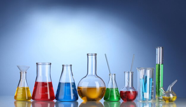 Diferentes vasijas de laboratorio con líquido de color y con reflejo sobre fondo azul
