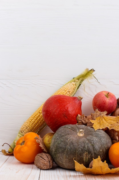 Diferentes vegetais, abóboras, maçãs, peras, nozes, milho, tomate e folhas secas em fundo branco de madeira. colheita de outono, copyspace.