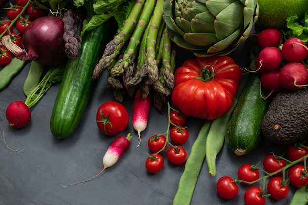 Diferentes vegetais orgânicos - espargos, tomate cereja, abacate, alcachofra, pimenta, limão, limão, sal em fundo cinza. fama alimentar com espaço de cópia, vista superior. conceito cru vegan vegetariano