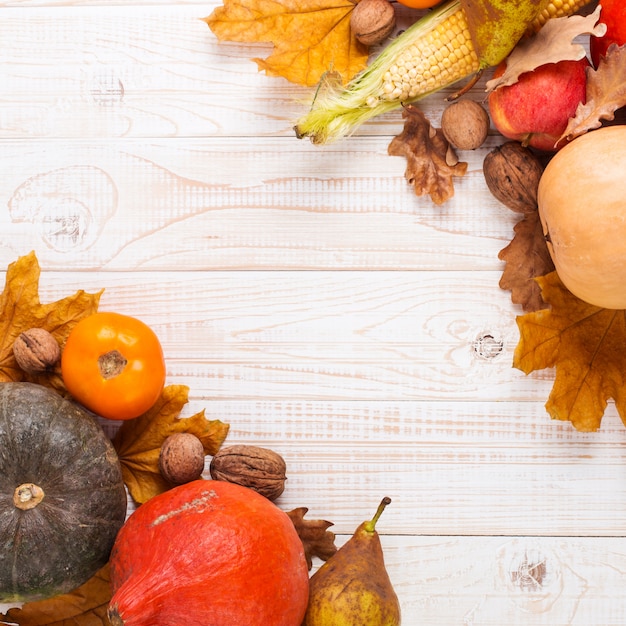 Diferentes verduras, calabazas, manzanas, peras, nueces, maíz, tomates y hojas secas sobre fondo blanco de madera. Cosecha de otoño, copyspace.