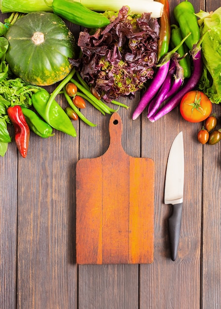 Diferentes verduras y tabla de cortar vacía con cuchillo de cocina de chef. Cocinar el concepto de comida sana. Vista superior. Copiar espacio