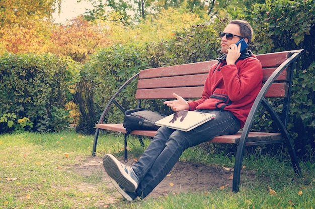 Difícil conversación de negocios por teléfono resolviendo problemas en el trabajo hombre insatisfecho trabajando en una computadora portátil Hablando por teléfono inteligente sentado en el parque descontento insatisfacción disgusto