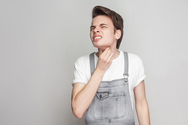 Difícil de engolir! Adolescente com dor de garganta e tocando o pescoço, pressionando os dedos nas glândulas, fechando os olhos para aliviar a dor com o rosto indefeso. Isolado, tiro de estúdio, copie o espaço em fundo cinza