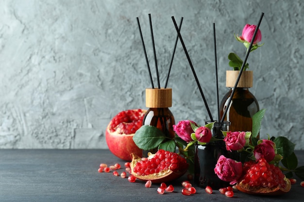 Difusores, flores y granada sobre mesa de madera oscura.