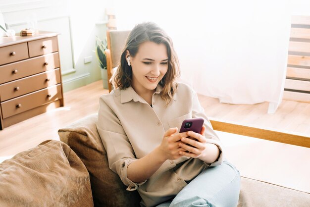 Digital Connection Delight Glückliche Millennial-Frau mit drahtlosen Kopfhörern schaut auf das Telefon und liest Unordnung