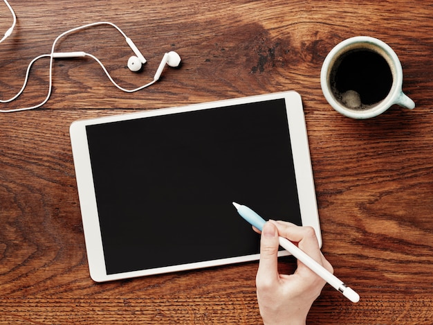 Digital tablet e xícara de café em uma mesa de madeira. lápis na mão.