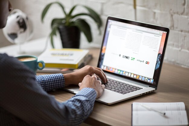 Digitaler Eingeborener lächelnder indischer Geschäftsmann arbeitet an einem Laptop in einem modernen Büro
