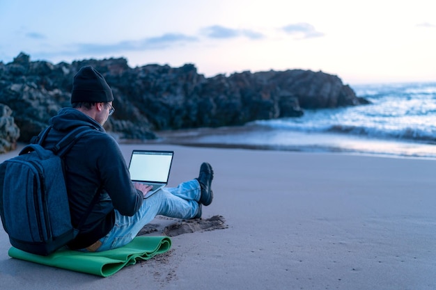 Digitaler Nomade, der draußen am Strand bei Sonnenuntergang an seinem Laptop arbeitet