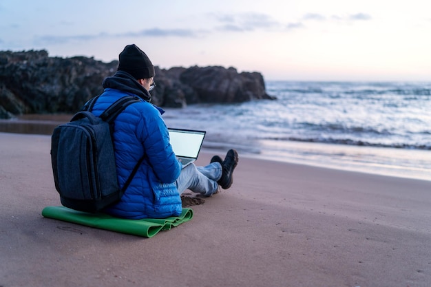 Digitaler Nomade, der draußen am Strand bei Sonnenuntergang an seinem Laptop arbeitet