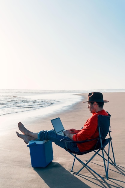 Digitaler Nomade, der mit Laptop am Ufer des Strandes sitzt und entspannt arbeitet