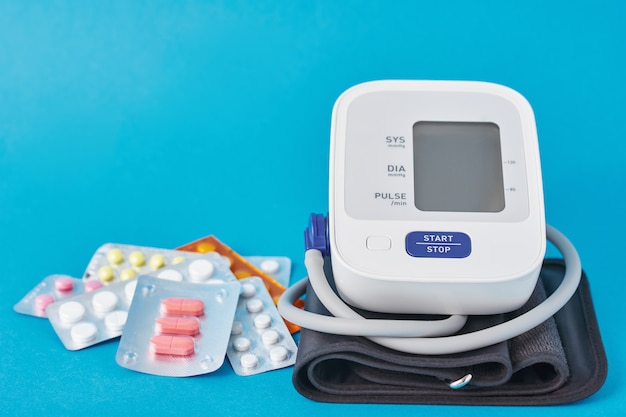 Digitales Blutdruckmessgerät und medizinische Pillen auf blauem Hintergrund. Gesundheits- und Medizinkonzept