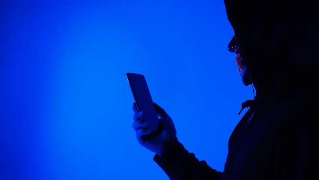 Digitales Sicherheitskonzept Anonymer Hacker mit Maske, die Smartphone hält, gehackt