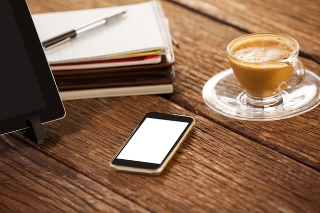 Digitales Tablet mit Smartphone und Tasse Kaffee auf Holztisch