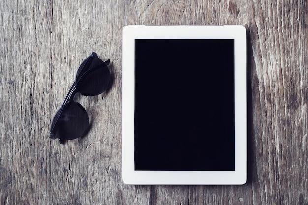 Digitales Tablet mit Sonnenbrille auf einem Holztisch