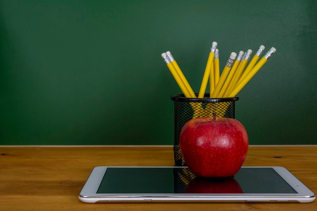 Digitales Tablet und Apple auf dem Schreibtisch vor der Tafel