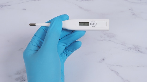 Digitales Thermometer weiße Farbe in den Händen des Arztes, die medizinische Handschuhe des Krankenhauses tragen hellblaue Farbe