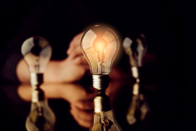Digitales zusammengesetztes Bild einer beleuchteten Glühbirne mit einer Person auf schwarzem Hintergrund