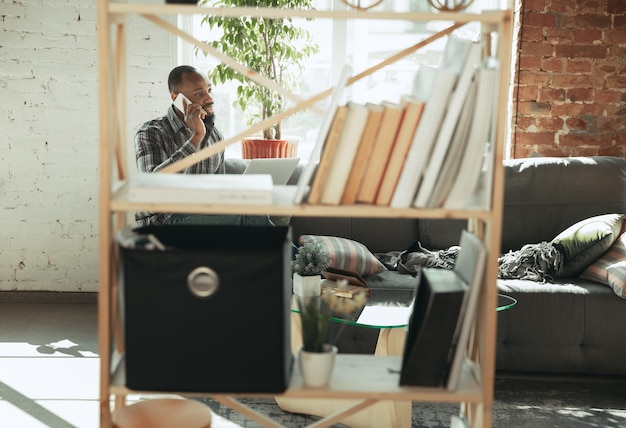 Foto digitando texto e falando no telefone. homem, freelancer durante o trabalho em home office durante a quarentena. jovem empresário em casa, auto-isolado. usando gadgets. trabalho remoto, prevenção de disseminação de coronavírus.