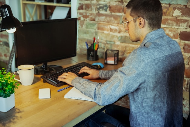 Digitando texto. homem que trabalha em casa durante a quarentena de coronavírus ou covid-19, conceito de escritório remoto. jovem empresário, gerente fazendo tarefas com smartphone, computador, tem conferência online, reunião.