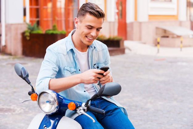 Digitando uma mensagem para um amigo. Jovem alegre sentado na scooter olhando para o celular