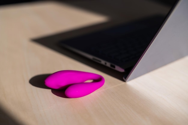 Dildo auf dem Tisch neben einem Laptop Das Konzept des Online-Sex Gebogene rosafarbener Vibrator für weibliche Selbstbefriedigung Stimulator für die Klitoris