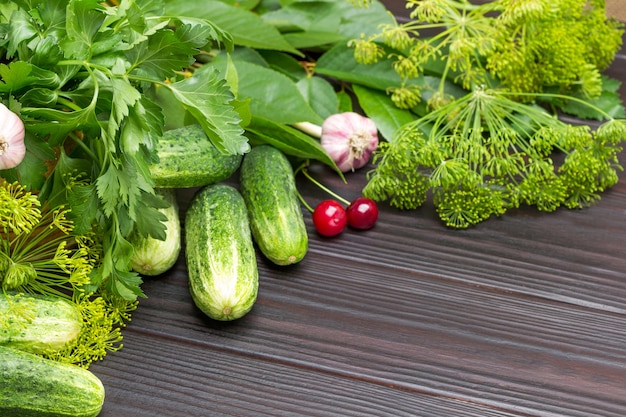 Dill- und Petersilienzweige, Gurken, Knoblauch und Kirschbeeren. Platz kopieren. Hölzerner Hintergrund. Ansicht von oben.