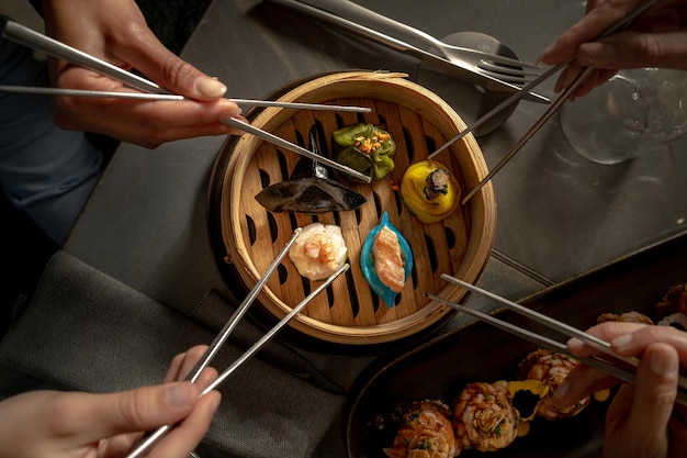 Dim sum no restaurante de fusão. Foto de topo plano com as mãos pegando os bolinhos com os pauzinhos.