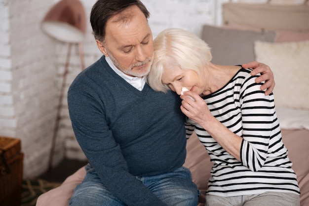 Dime por qué. La señora mayor muy triste está llorando y apoyada en el hombro de su marido.