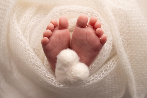 El diminuto pie de un bebé recién nacido. Pies suaves de un recién nacido en una manta de lana blanca. Primer plano de los dedos de los pies, los talones y los pies de un recién nacido. Corazón blanco tejido en las piernas de un bebé. Fotografía macro.