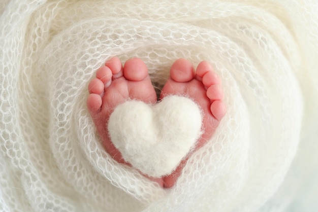 El diminuto pie de un bebé recién nacido Pies suaves de un recién nacido en una manta de lana blanca Primer plano de los dedos de los pies, talones y pies de un recién nacido Corazón blanco tejido en las piernas de un bebé Fotografía macro