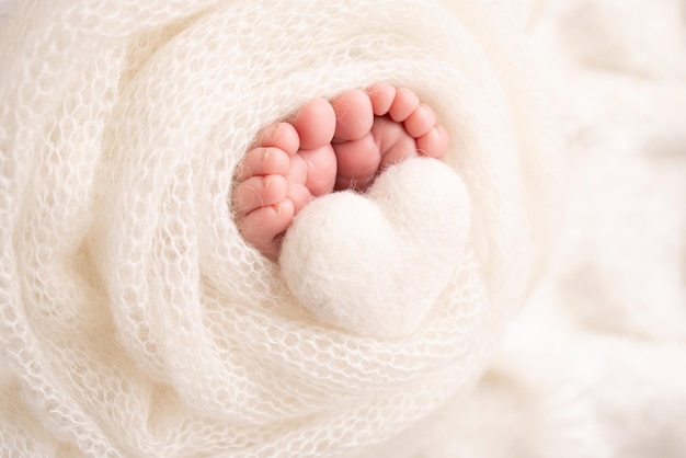 El diminuto pie de un bebé recién nacido Pies suaves de un recién nacido en una manta de lana blanca Primer plano de los talones de los dedos de los pies y los pies de un recién nacido Corazón blanco de punto en las piernas de un bebé Fotografía macro