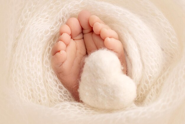 El diminuto pie de un bebé recién nacido Pies suaves de un recién nacido en una manta de lana blanca Primer plano de los talones de los dedos de los pies y los pies de un recién nacido Corazón blanco de punto en las piernas de un bebé Fotografía macro