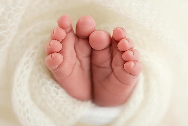 El diminuto pie de un bebé recién nacido Pies suaves de un recién nacido en una manta de lana blanca Primer plano de los talones de los dedos de los pies y los pies de un recién nacido Corazón blanco de punto en las piernas de un bebé Fotografía macro