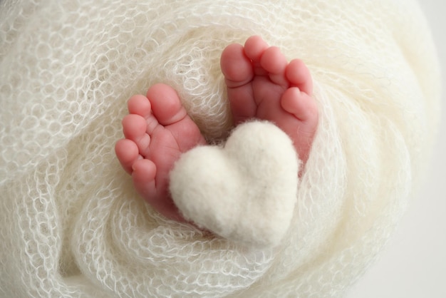 El diminuto pie de un bebé recién nacido Pies suaves de un recién nacido en una manta de lana blanca Primer plano de los talones de los dedos de los pies y los pies de un recién nacido Corazón blanco de punto en las piernas de un bebé Fotografía macro