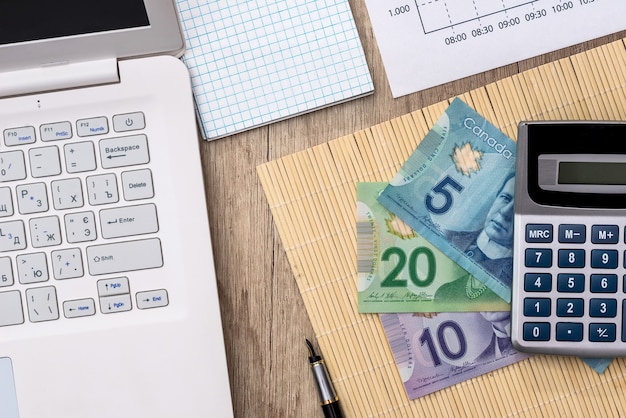 Dinero canadiense con computadora portátil, documento, bandeja y calculadora