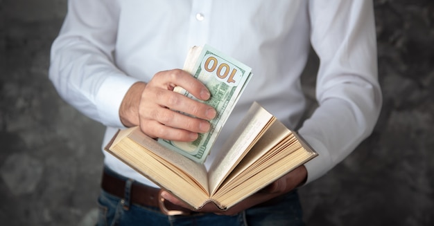 Foto dinero de la mano del hombre en el libro sobre fondo oscuro