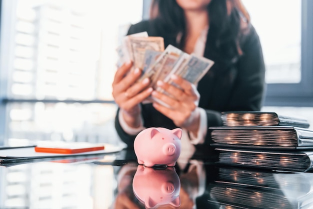 Foto con dinero mujer en ropa formal negra está en el interior de la oficina moderna