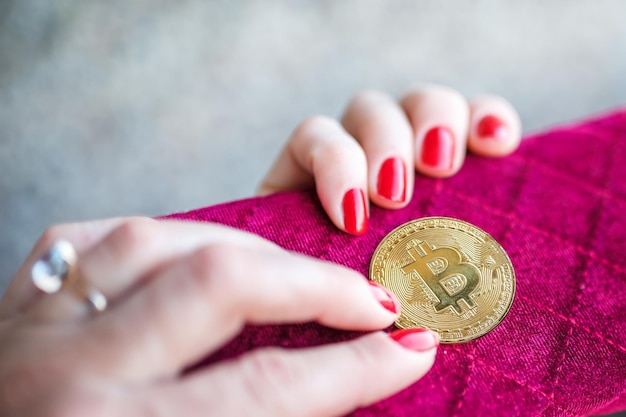 Dinero virtual bitcoin dorado en dedos de monedero de tela de mujer rosa con uñas rojas en una moneda