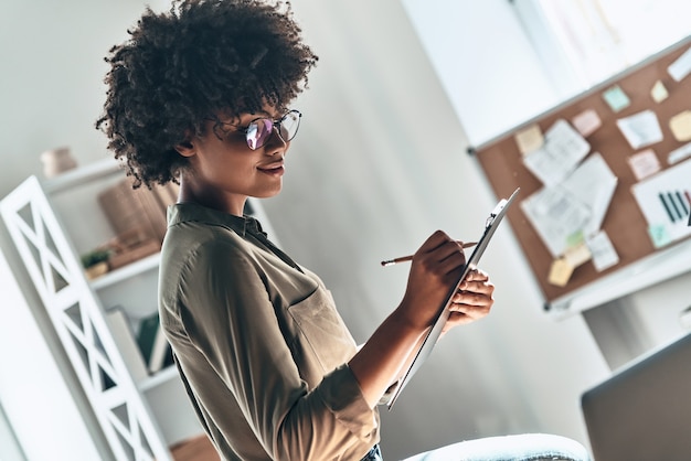 Dinge erledigen. Attraktive junge Afrikanerin, die während der Arbeit im Büro etwas aufschreibt