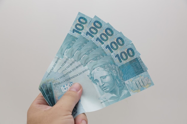 Dinheiro de cem reais brasileiros na mão de uma pessoa segurando