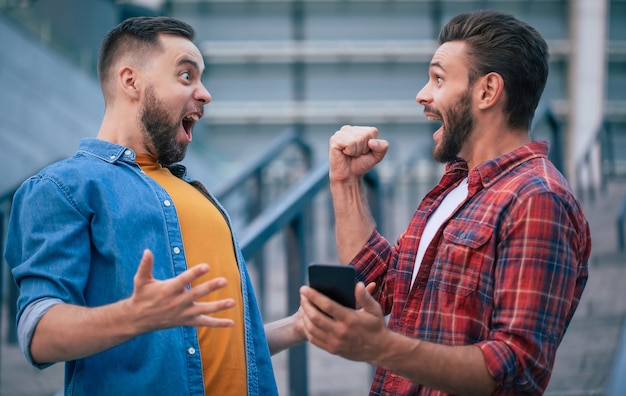 Foto dinheiro e apostas online. melhores amigos modernos felizes e animados com telefone inteligente estão gritando e erguem os punhos para ganhar algum jogo