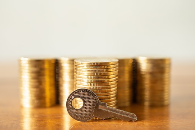 Dinheiro financeiro e conceito de segurança. close-up da chave com uma pilha de moedas de ouro na mesa de madeira.