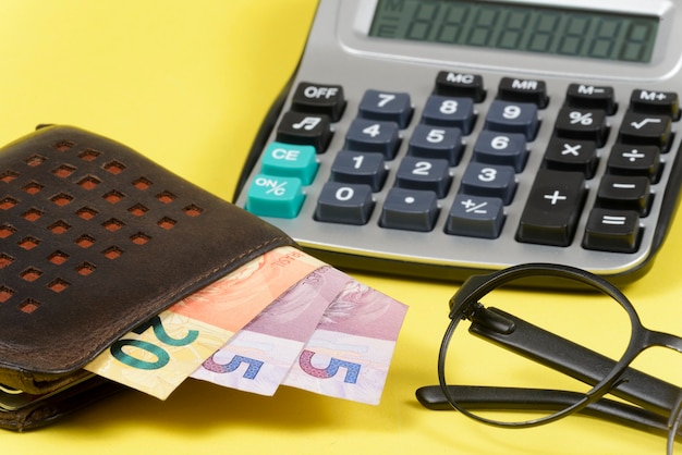 Dinheiro saindo da carteira com calculadora de bolso desfocada