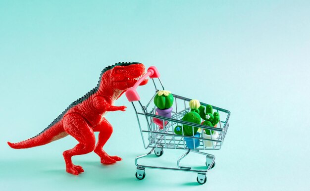 Dinosaurio rojo con carrito de compras lleno de cactus sobre fondo azul.