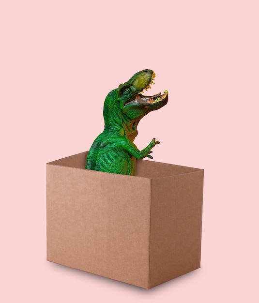 Foto un dinosaurio verde gracioso sale de una caja de cartón sobre un fondo rosado una tarjeta de felicitación minimalista graciosa