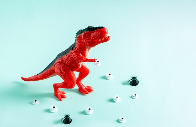 Dinossauro de brinquedo vermelho com xícaras de café e cafeteira em fundo azul Conceito de dependência de café