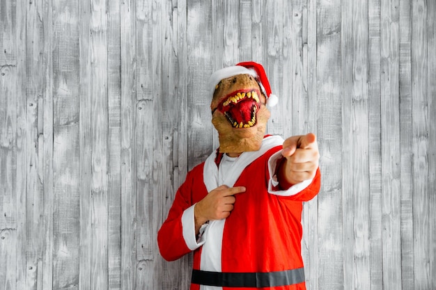 Dinossauro fantasiado de Papai Noel apontando o dedo para a câmera.